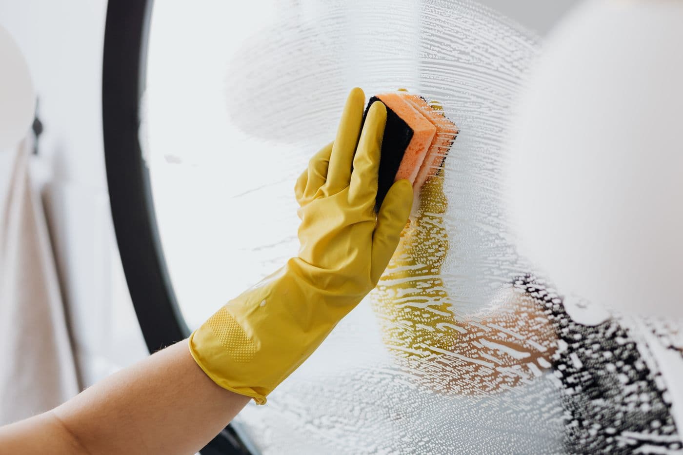 Nettoyage à la mousse d'un miroir de salle de bains, gant jaune et éponge